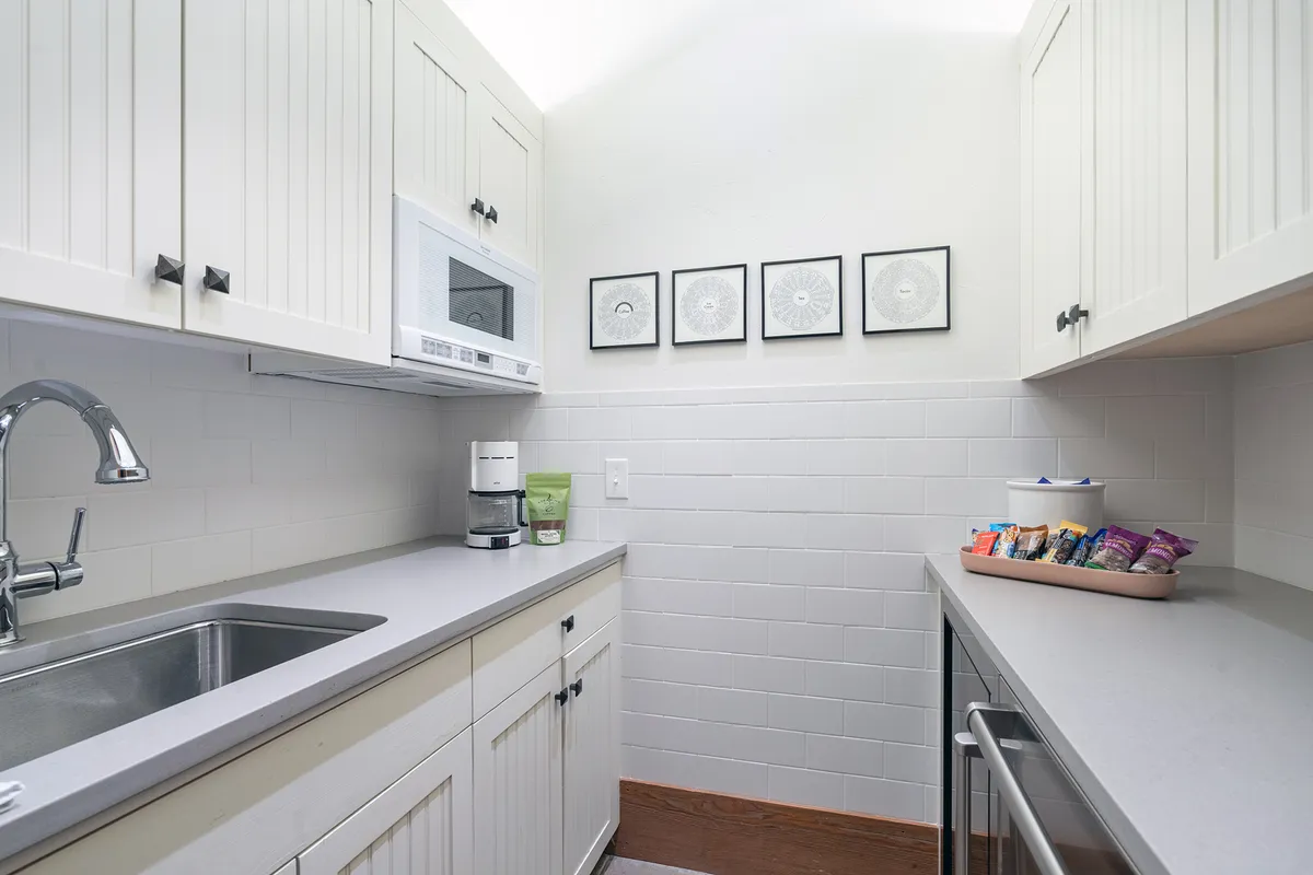 A functional and welcoming kitchen view with a snack tray on the counter, a microwave, kitchen sink, and art on the wall. The setup encourages casual snacking, meal prepping, and socializing in a communal zone.