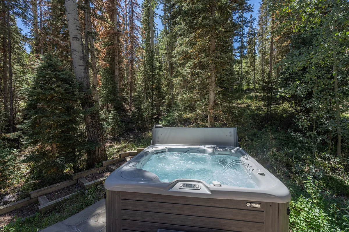 A serene outdoor hot tub nestled among tall pines in a forested setting. The tub is surrounded by natural landscaping and offers a tranquil space for relaxation, with the forest providing privacy and a deep sense of immersion in nature.