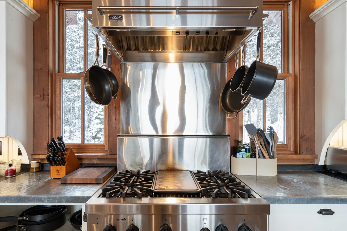 A warm, functional kitchen scene with a stainless steel stove, hanging pots, and large windows letting in natural light. The space is inviting, ideal for cooking and sharing meals together after a day of adventure.