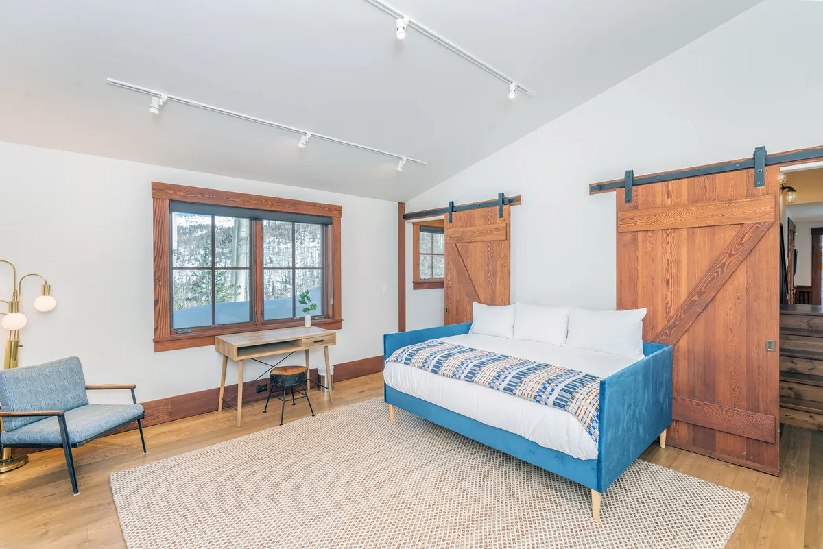 A tranquil day bed nook nestled by large windows, with wooden sliding doors and a desk nearby. The nook is bright and inviting, perfect for lounging, reading, or enjoying the scenery.