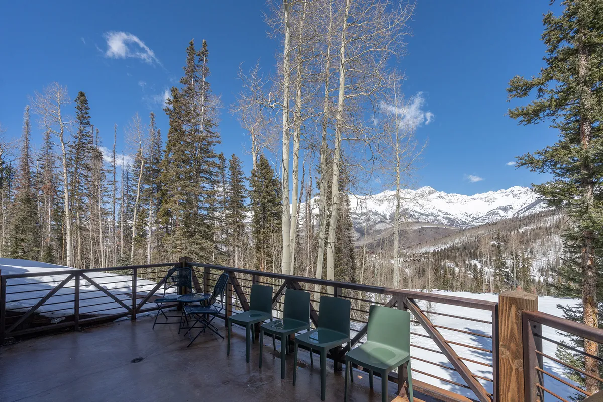 An exterior view showing a snow-covered mountain landscape as seen from a wooden deck or balcony, with empty chairs positioned to take in the view. The serene outdoor setting invites moments of reflection or relaxation after work.