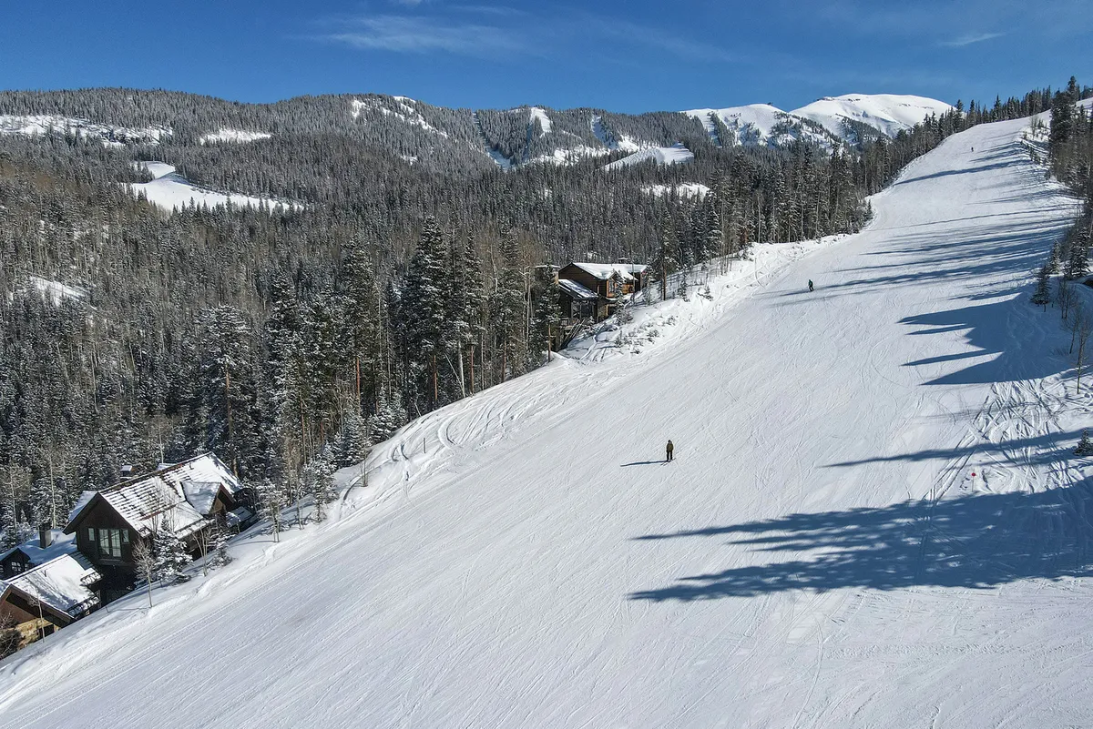 A panoramic view of snow-covered slopes dotted with skiers and mountain cabins, framed by evergreen trees. The dynamic activity and stunning vistas showcase the allure of the region’s winter sports.