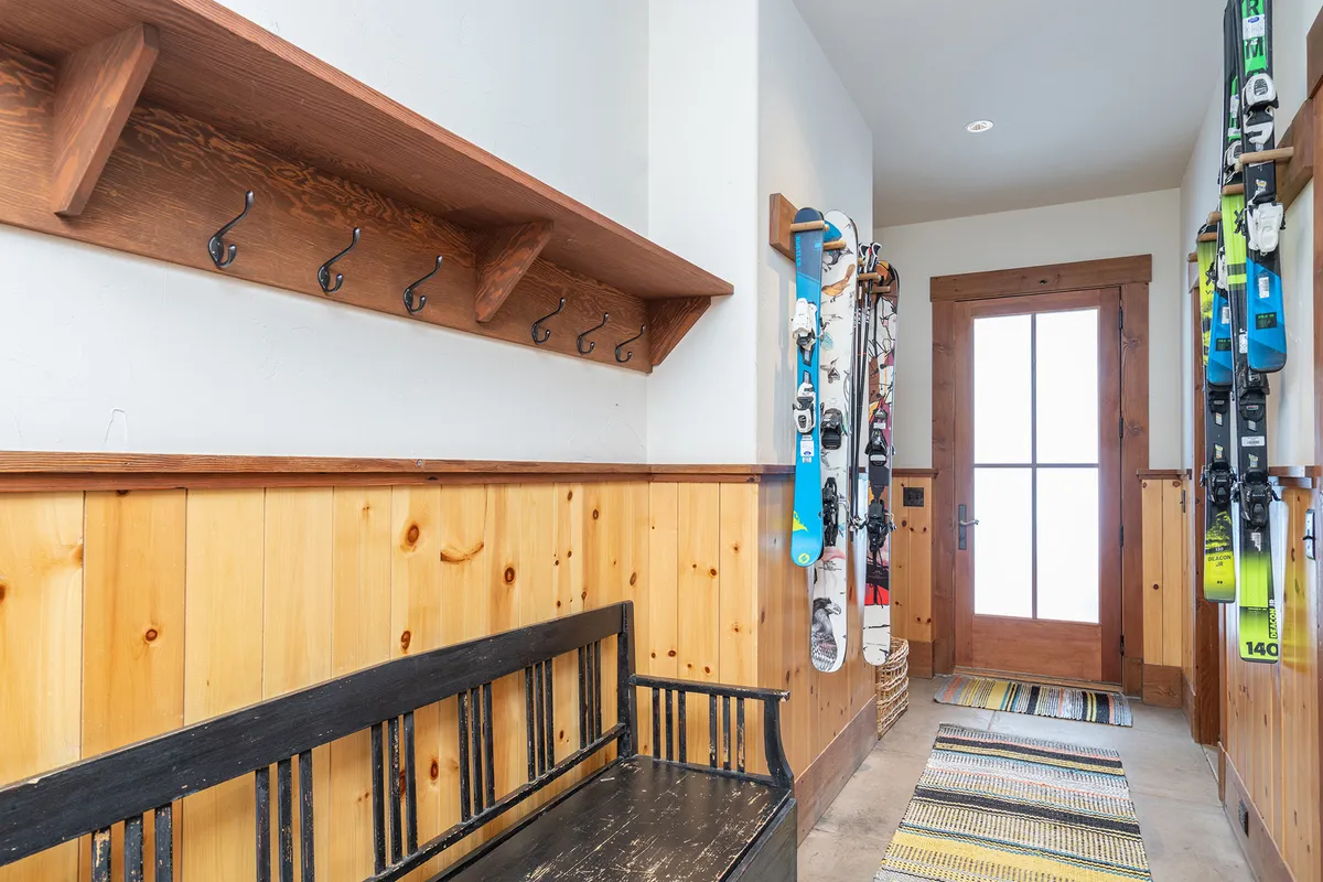 A mudroom designed for ski and gear storage, featuring a wooden bench, ski equipment, hooks on the wall, and the front door nearby. The space is cozy, organized, and clearly tailored for those returning from outdoor adventures.