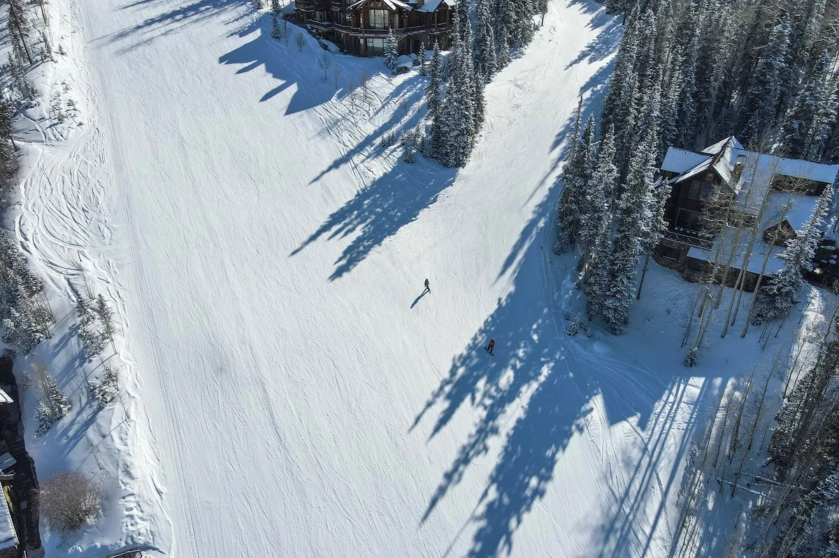A lively ski slope scene featuring skiers gliding down snow-covered runs bordered by frosty trees, with luxurious lodges visible in the background. The early morning light casts a soft glow on the white landscape, evoking the thrill and accessibility of the slopes.