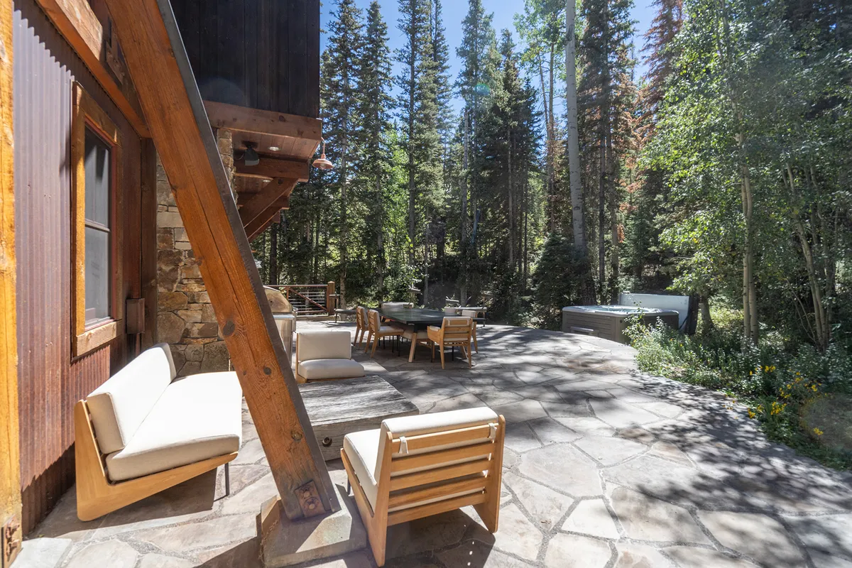 A spacious wooden deck surrounded by trees, featuring an outdoor seating area and a large dining table. The setting is tranquil and inviting, suggesting spaces for relaxation and shared meals after a day of outdoor adventure.