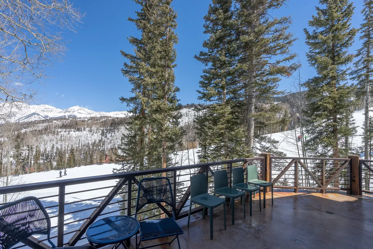 A serene balcony with comfortable seating overlooks snow-covered mountains and tall pines, offering a tranquil spot to unwind and soak in the surrounding alpine beauty.